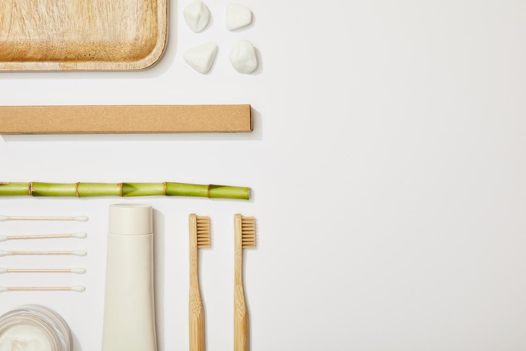 竹の歯ブラシ、歯磨き粉のチューブ、化粧品クリーム、石、耳棒、竹の幹の白い背景の上の平面図 - 写真・画像