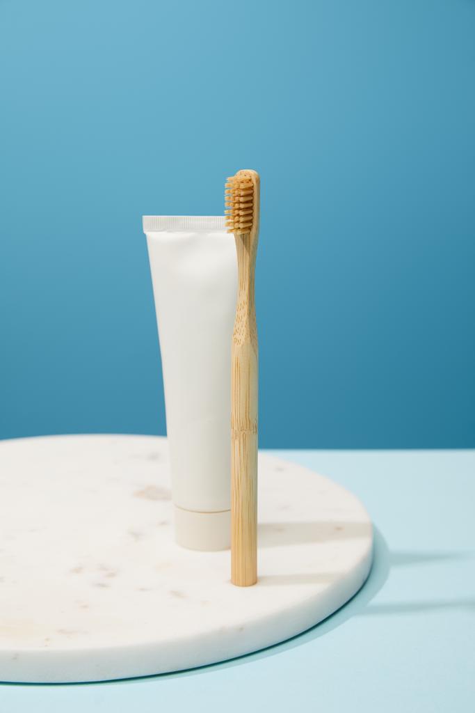 weiße Marmorplatte mit Bambus-Zahnpasta in Tube und Zahnbürste auf blauem Hintergrund - Foto, Bild