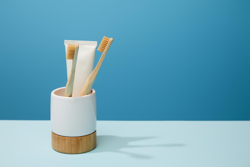 supporto con dentifricio in tubo e spazzolini in bambù su tavolo e fondo blu
 - Foto, immagini