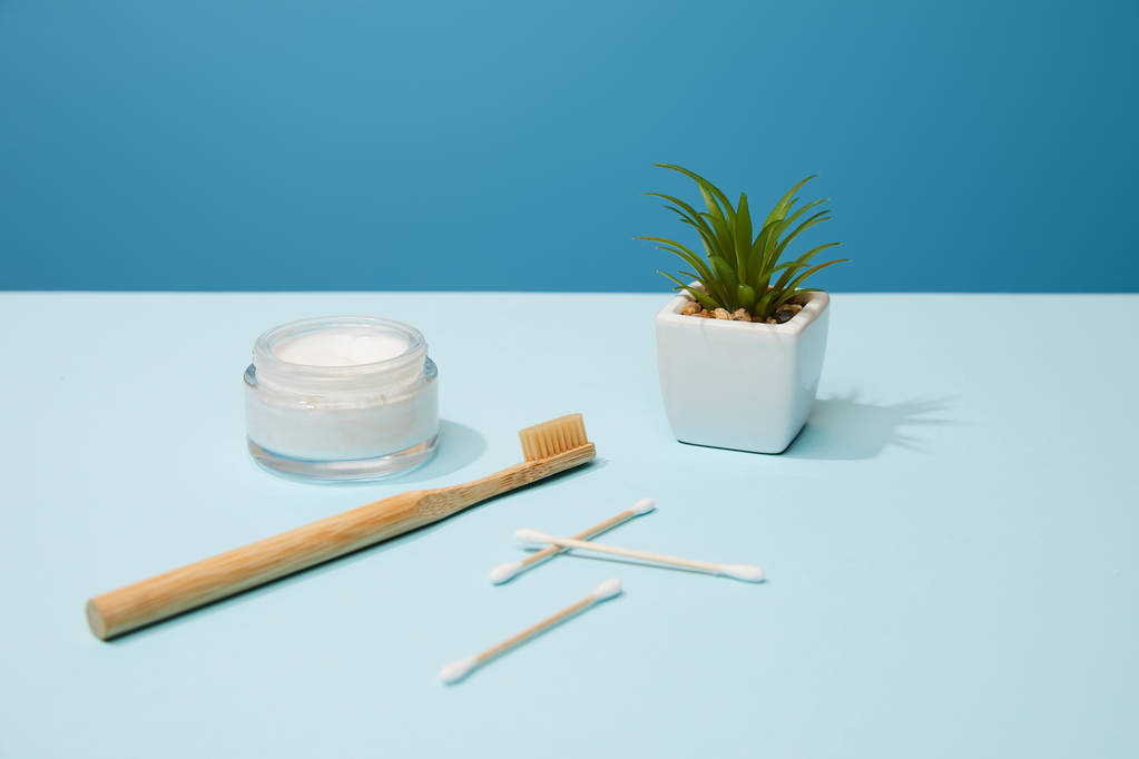 Cepillo de dientes de bambú, crema cosmética y planta en maceta sobre mesa y fondo azul
 - Foto, imagen