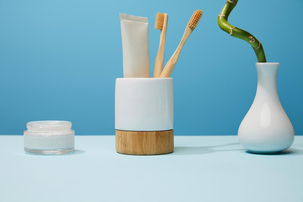 soporte para cepillos de dientes, crema cosmética y tallo de bambú sobre mesa y fondo azul
 - Foto, imagen