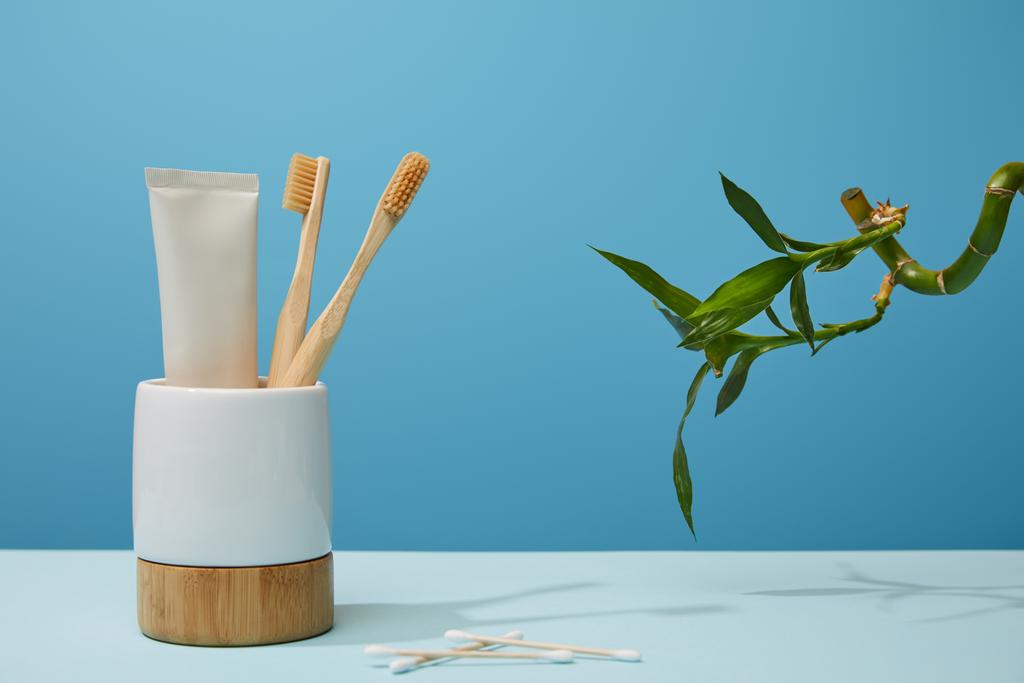 support avec brosses à dents, dentifrice en tube, bâtons d'oreille et tige de bambou vert sur table et fond bleu
 - Photo, image