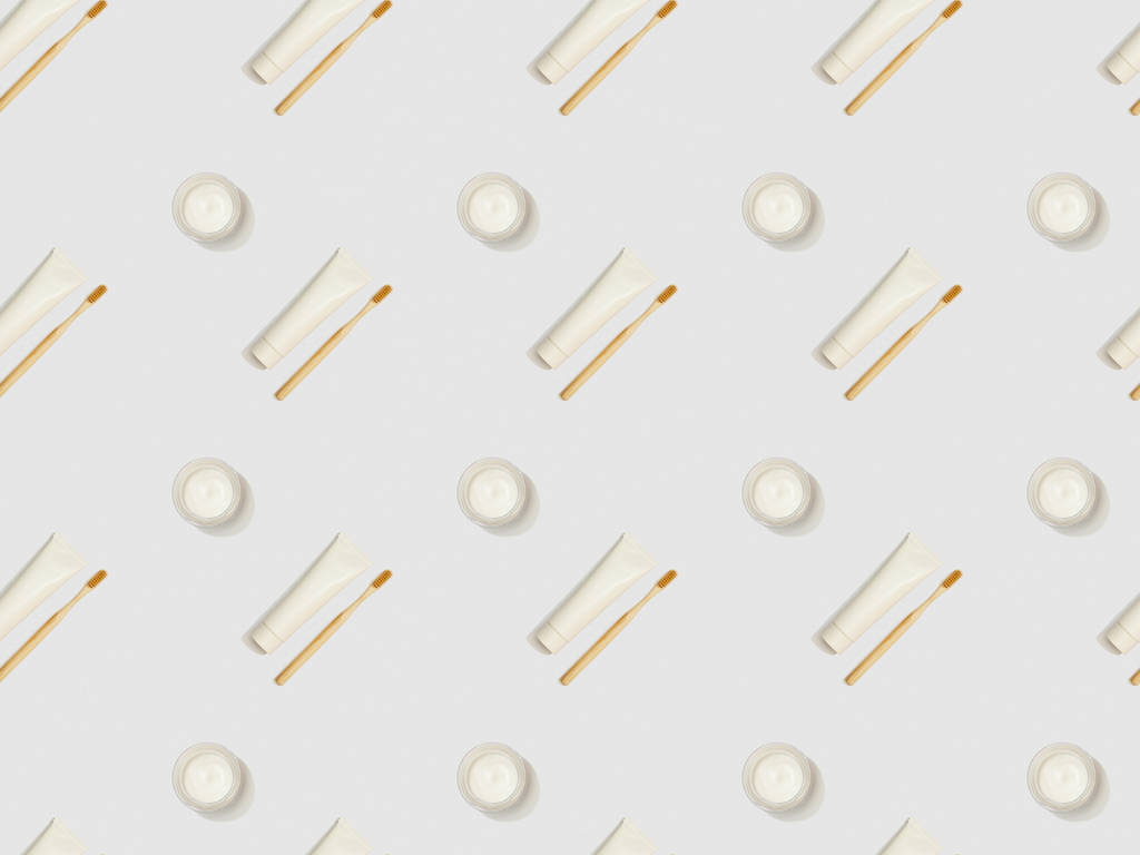 diagonaal gelegen bamboe tandenborstels, tandpasta in buizen en cosmetische crème op grijze achtergrond, naadloze achtergrondpatroon - Foto, afbeelding