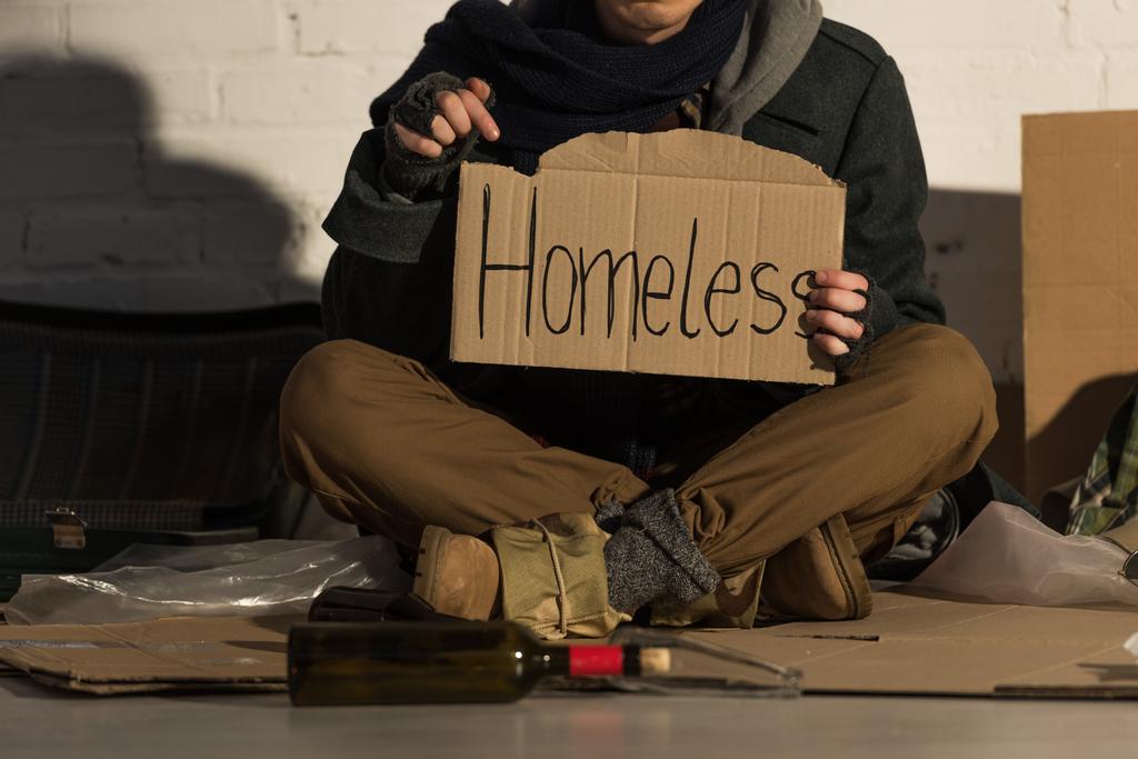 weergave van dakloze man houdt stuk karton met "de dakloze" handgeschreven inscriptie bijgesneden - Foto, afbeelding