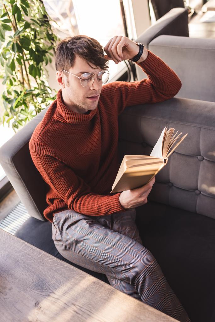 στοχαστικός άνθρωπος σε γυαλιά ανάγνωσης βιβλίο ενώ κάθονται στην καφετέρια - Φωτογραφία, εικόνα