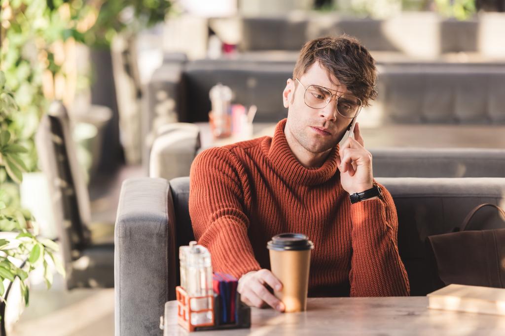 selektiivinen painopiste vakava mies lasit puhuu älypuhelimeen lähellä paperi kuppi kahvia ja kirjaa
  - Valokuva, kuva