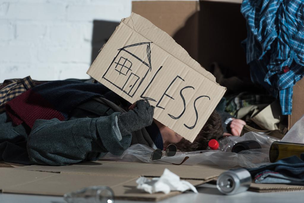 sans-abri couché sur des ordures humides avec le symbole de la maison et "moins" lettrage sur carte de carton
 - Photo, image