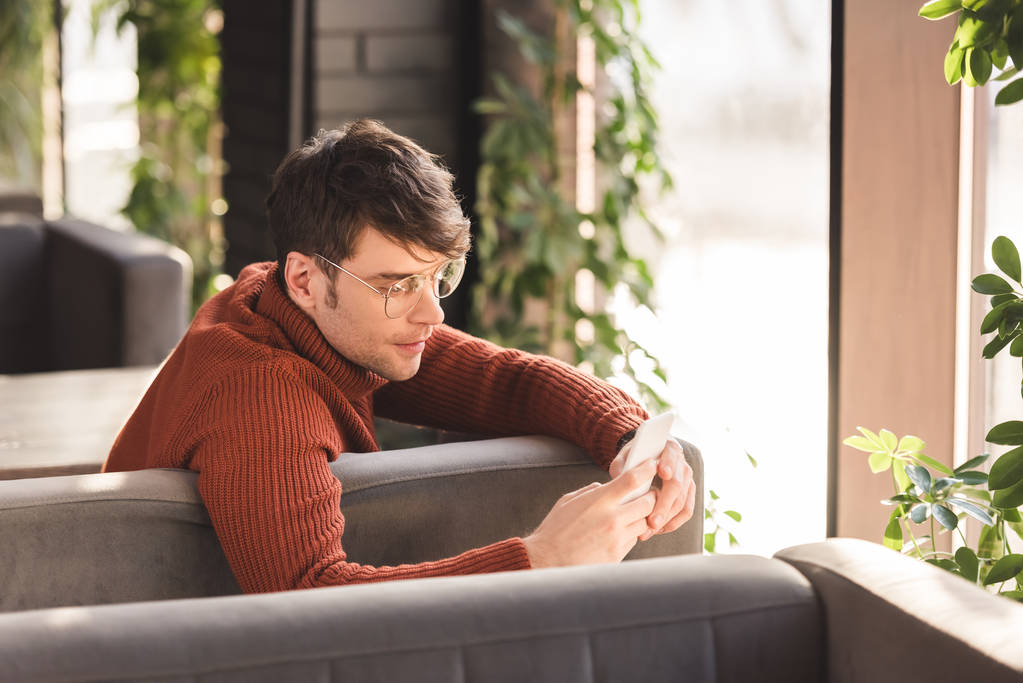 jovem sério em óculos usando smartphone enquanto sentado no café
 - Foto, Imagem