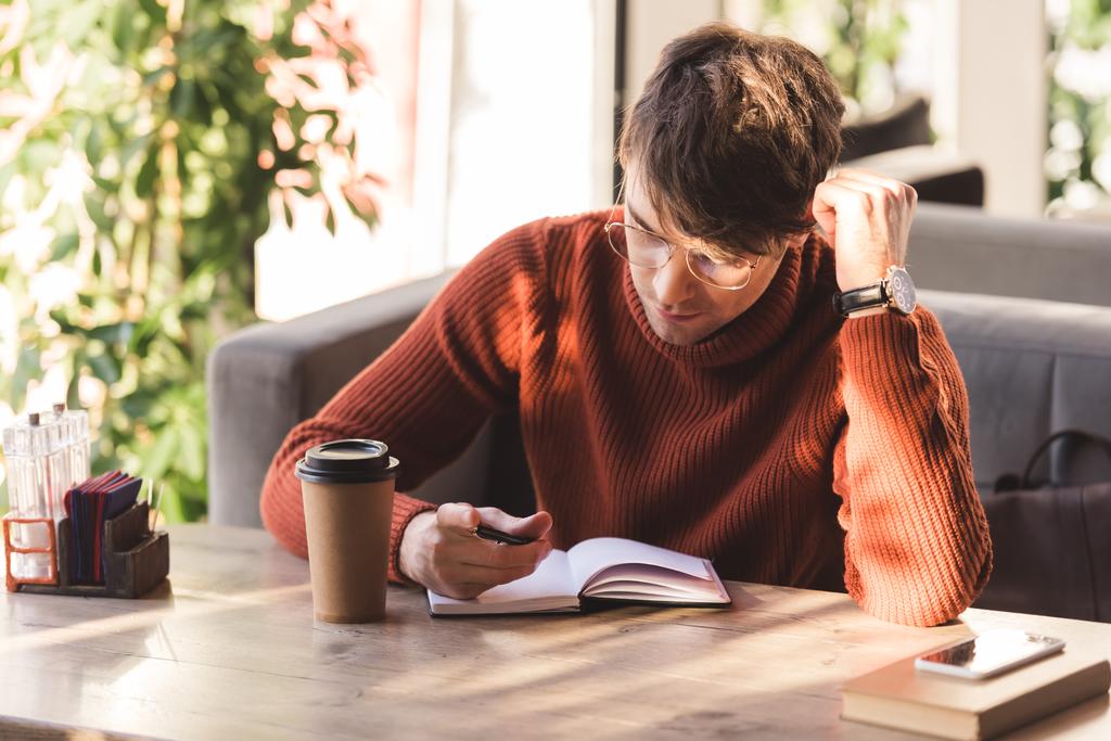 bel homme dans des lunettes regardant cahier près de tasse jetable dans le café
 - Photo, image