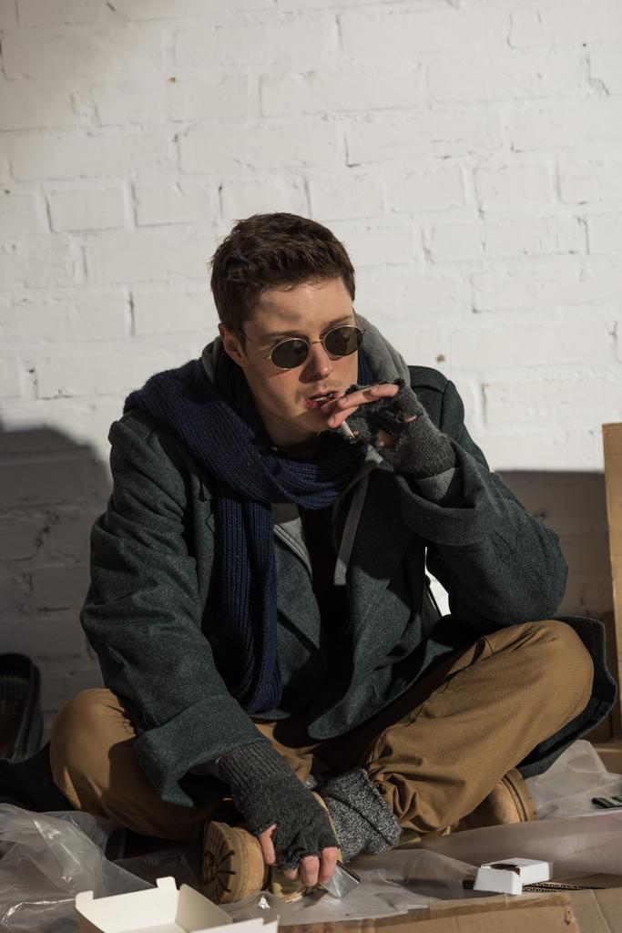 hajléktalan férfi dohányzás cigaretta ülve, fehér tégla fal - Fotó, kép