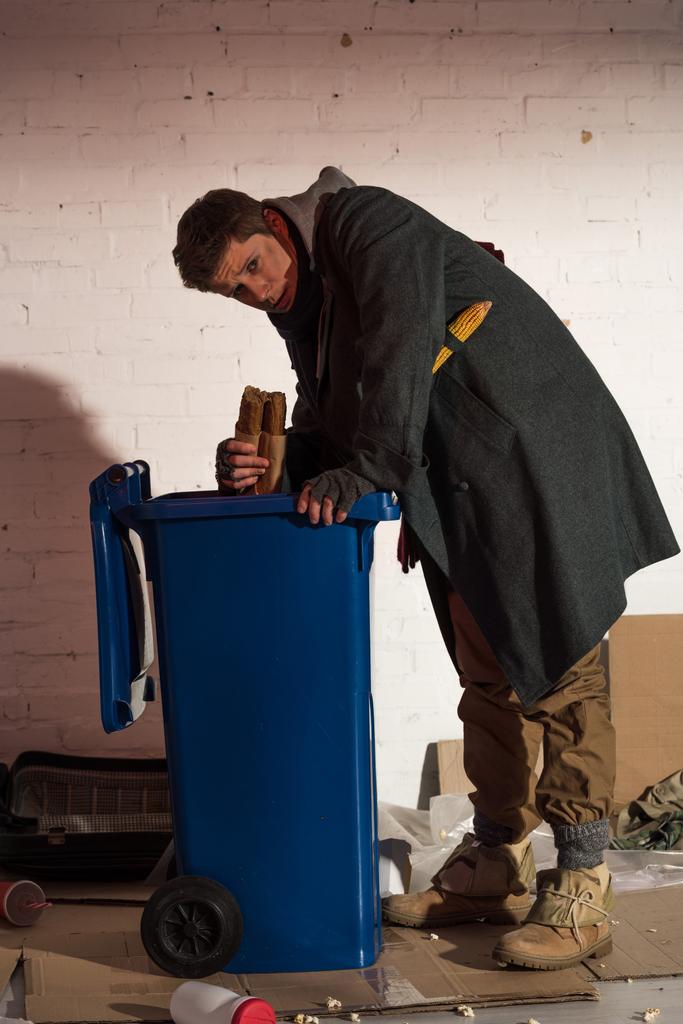 Hungriger Obdachloser holt Baguette aus Müllcontainer - Foto, Bild