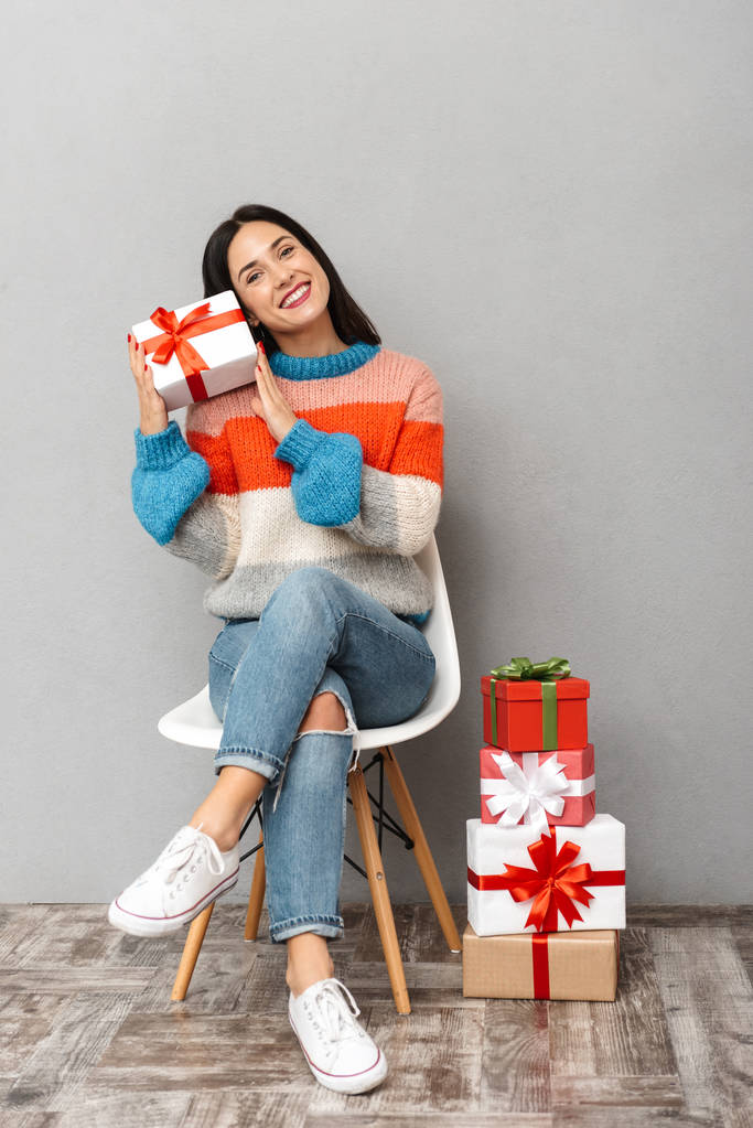 Photo de femme heureuse 30s assis dans une chaise avec des boîtes cadeaux isolés sur fond gris
 - Photo, image