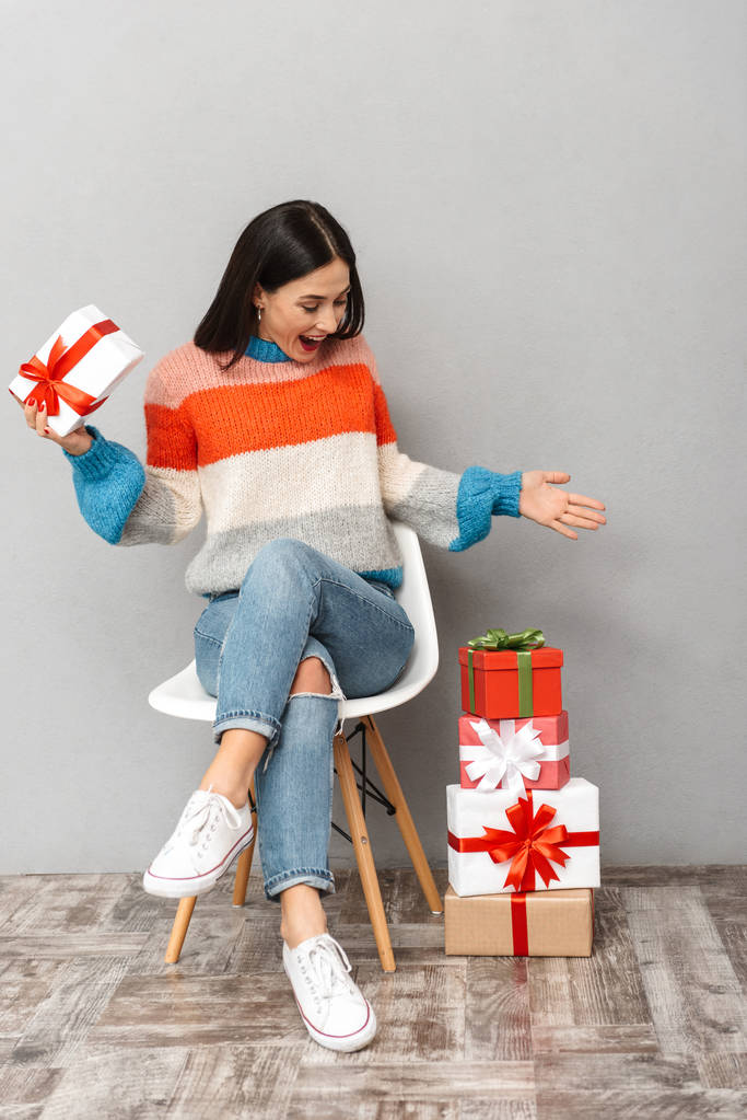 Photo of stylish woman 30s sitting in chair with present boxes isolated over gray background - Photo, Image