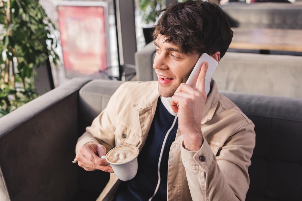 счастливый человек держит чашку с капучино и говорить на смартфоне в кафе
 - Фото, изображение