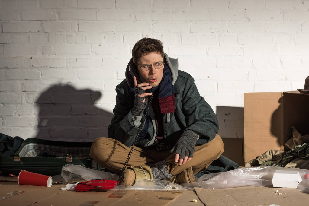 bezdomovec pomocí vintage telefonní zatímco sedí na skládce - Fotografie, Obrázek