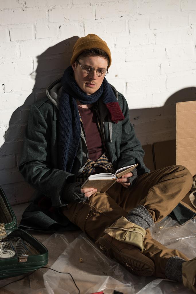 bezdomnego, czytanie książki siedząc przez biały mur  - Zdjęcie, obraz
