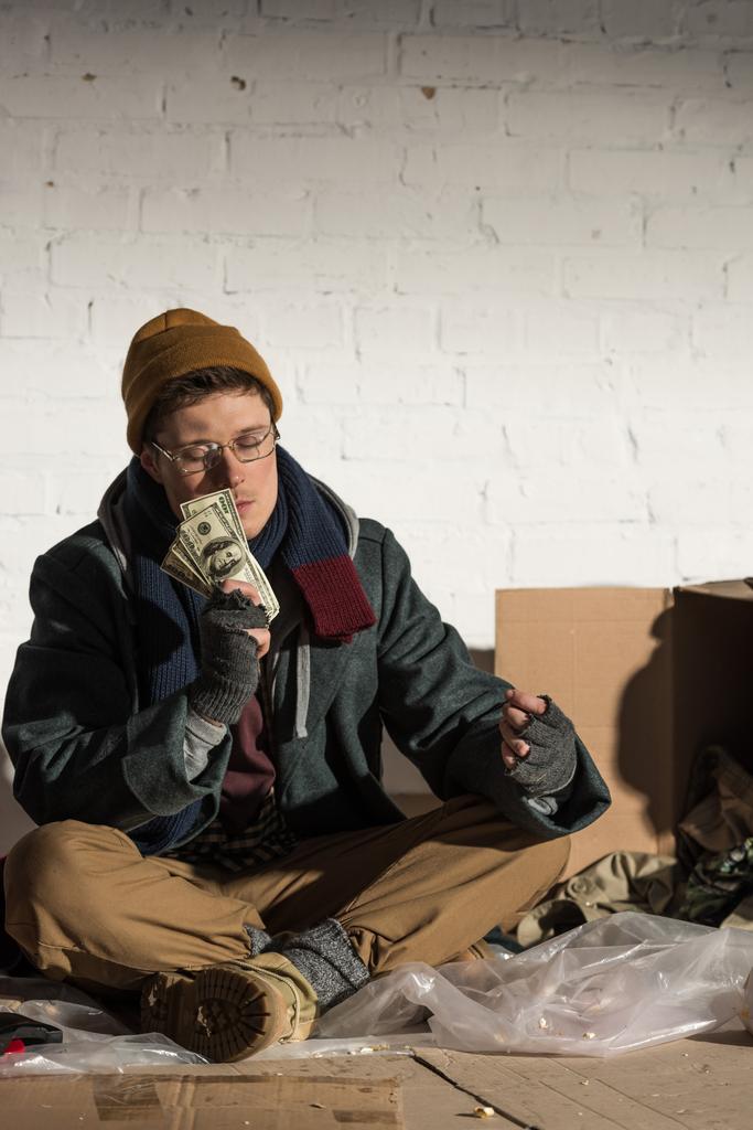 Um sem-abrigo sentado na lixeira e a segurar dinheiro
 - Foto, Imagem