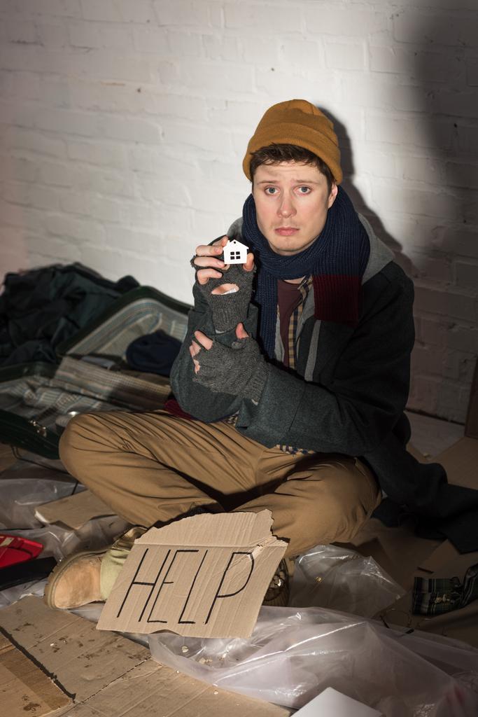deprimido hombre sin hogar sentado cerca de la tarjeta de cartón con "ayuda" texto escrito a mano y sosteniendo casa de papel cortado
 - Foto, Imagen