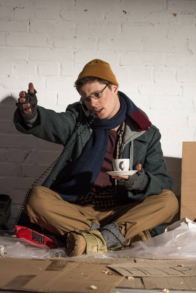 Obdachloser hält Kaffeetasse in der Hand und benutzt Handy - Foto, Bild