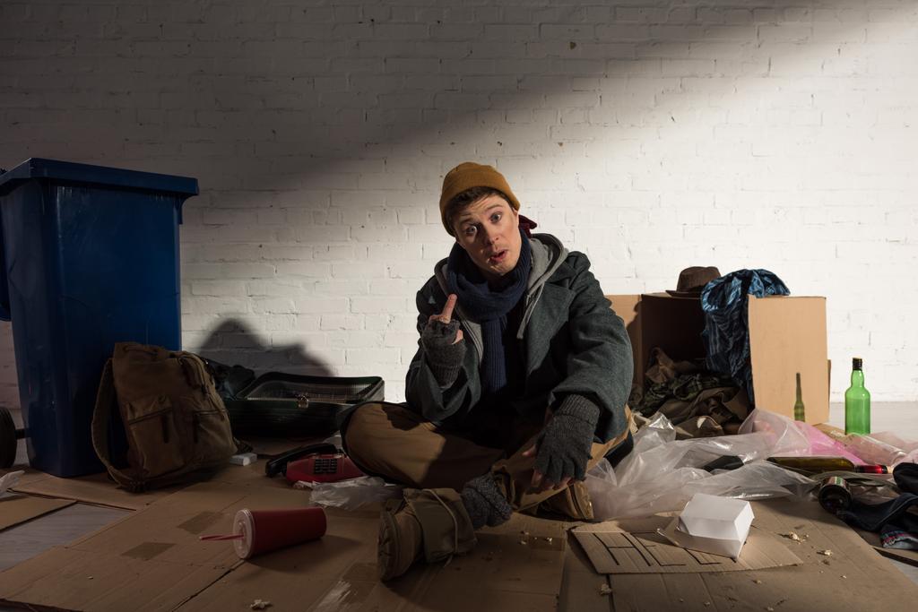 Obdachloser zeigt Mittelfinger während er auf Müllhalde sitzt - Foto, Bild