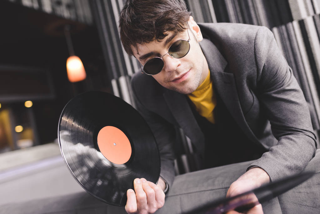 schöner junger Mann mit Sonnenbrille schaut auf Retro-Schallplatten - Foto, Bild