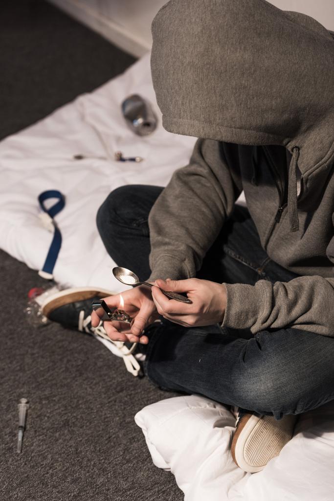 junkie man in hood heating spoon with heroin on lighter - Photo, Image