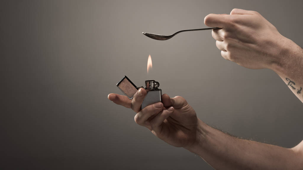 oříznutý pohled na člověka feťák topení lžíce s heroinem na zapalovač na šedém pozadí - Fotografie, Obrázek