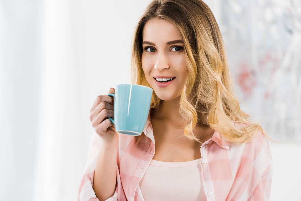 Blissful beautiful woman looking at camera and drinking coffee - Photo, Image