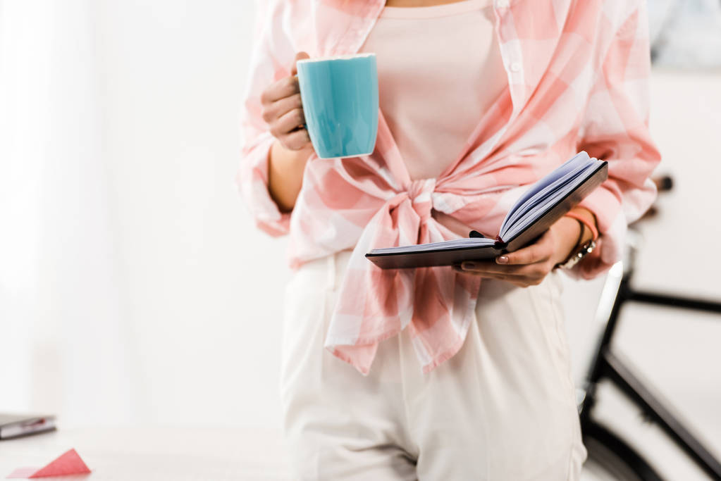 Vista parcial de la mujer sosteniendo el cuaderno y bebiendo café
 - Foto, imagen