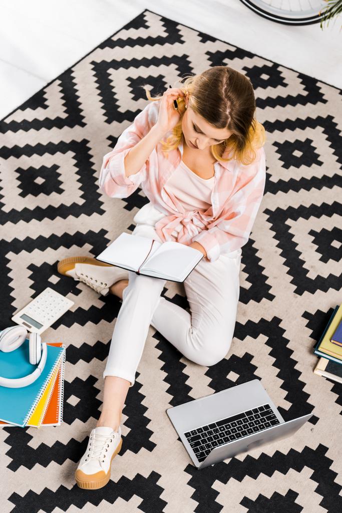 Elfoglalt lány fehér nadrág, ül a szőnyegen, és a gazdaság notebook - Fotó, kép