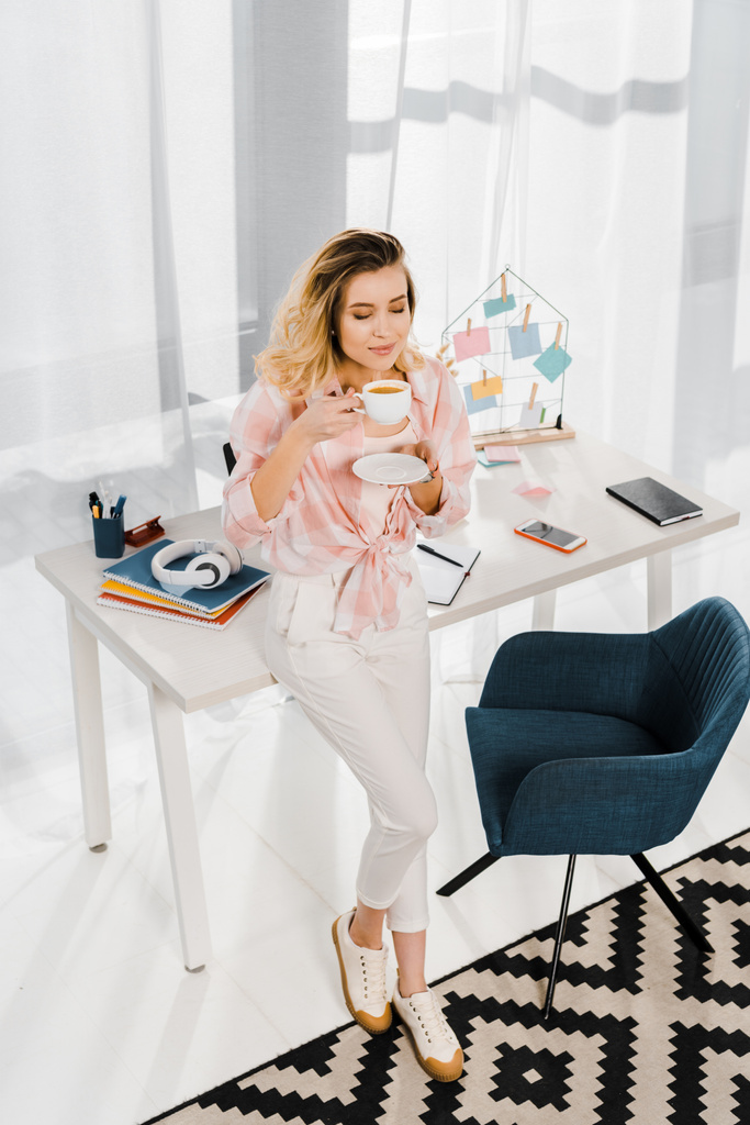 Donna rilassata in camicia a scacchi bere caffè con gli occhi chiusi sul posto di lavoro
 - Foto, immagini