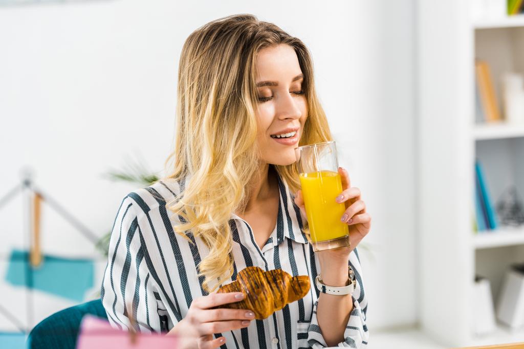 Femme détendue en chemise rayée tenant croissant et boire du jus d'orange
 - Photo, image