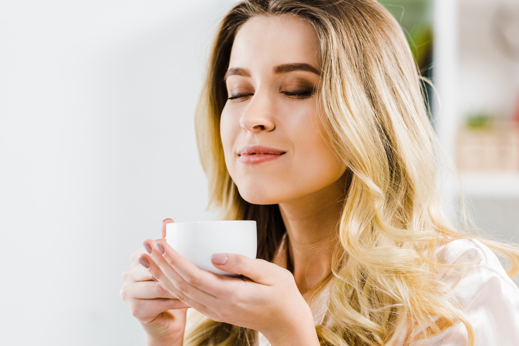 Uvolněná mladá žena držící šálek kávy se zavřenýma očima - Fotografie, Obrázek