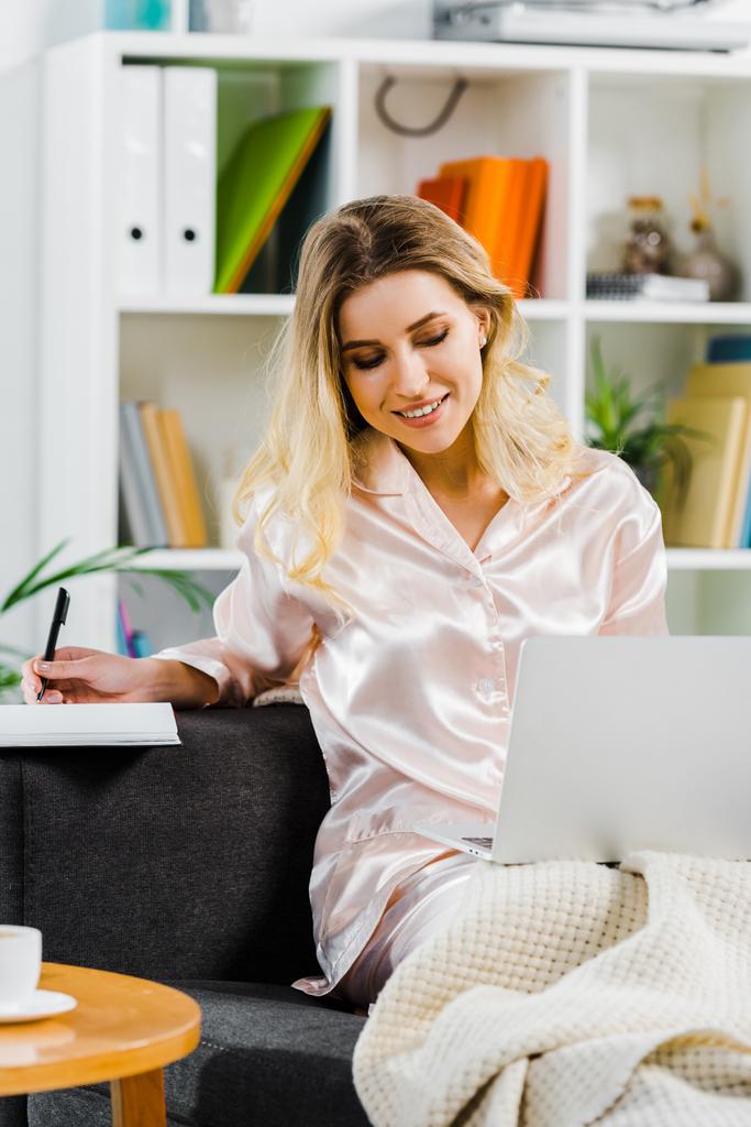 Kaunis nainen pyjamassa kannettavan tietokoneen avulla ja kirjoittamalla kannettavaan kotona
 - Valokuva, kuva