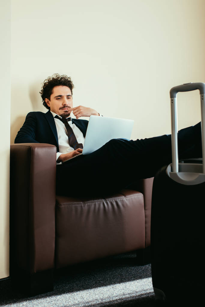 homme d'affaires en costume travaillant sur ordinateur portable avec les jambes sur la valise dans la chambre d'hôtel
 - Photo, image