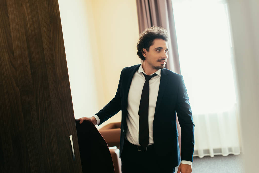 schöner Geschäftsmann nimmt Kleidung aus Kleiderschrank im Hotelzimmer - Foto, Bild