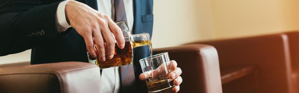 przycięte widzenia biznesmen wylewanie whisky z butelki do szkła w pokoju hotelowym  - Zdjęcie, obraz