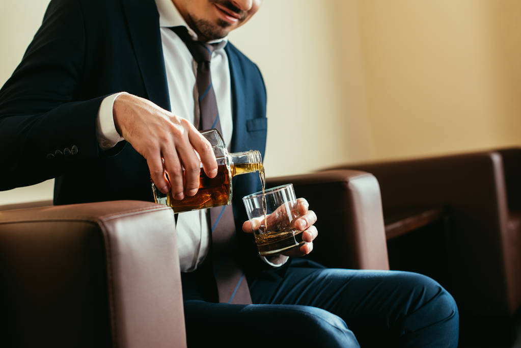 vista recortada del hombre de negocios vertiendo whisky en el vidrio en la habitación de hotel
  - Foto, imagen