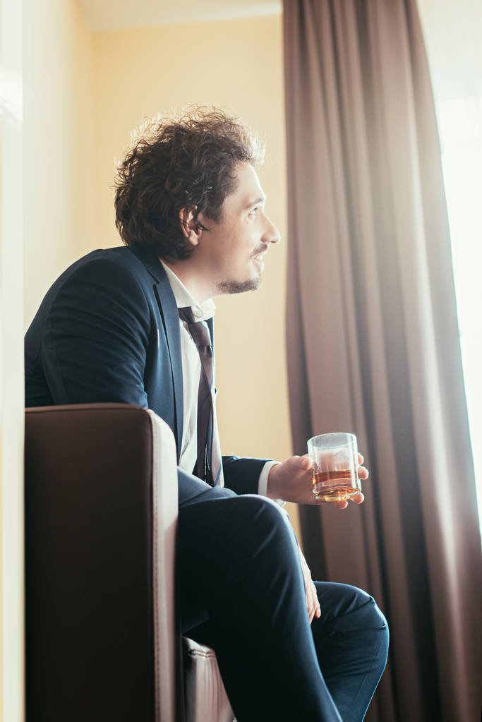 ονειρική επιχειρηματία στο κοστούμι κρατώντας το ποτήρι ουίσκι στο δωμάτιο του ξενοδοχείου  - Φωτογραφία, εικόνα