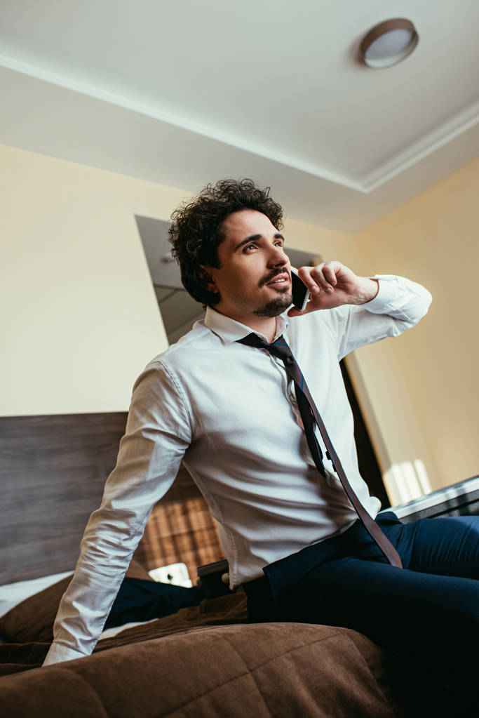 guapo hombre de negocios en ropa formal hablando en el teléfono inteligente en la habitación de hotel
 - Foto, imagen