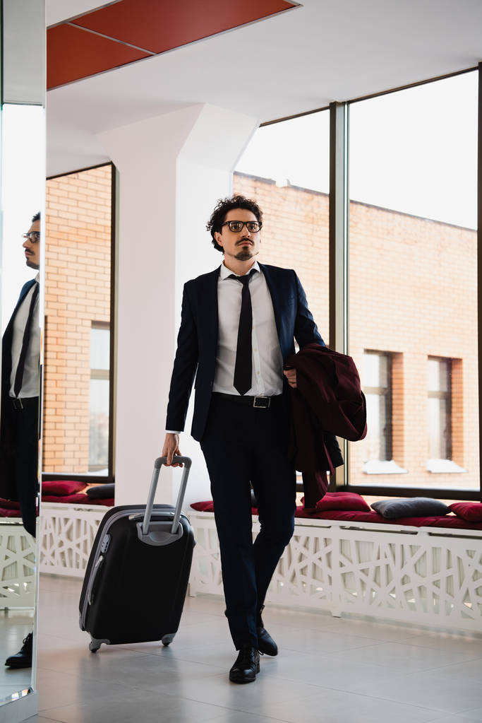 hombre de negocios en traje caminando en el vestíbulo del hotel con bolsa de viaje
 - Foto, imagen