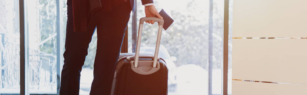 vista recortada de hombre de negocios con pasaporte y equipaje que llega al hotel con luz solar
 - Foto, Imagen