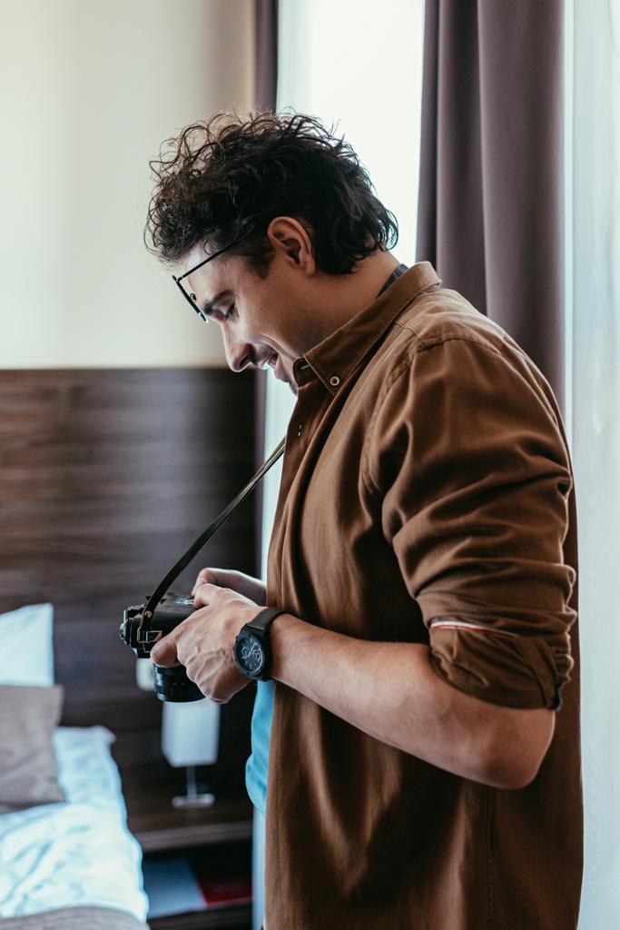fotógrafo sorridente em óculos olhando para a câmera fotográfica no quarto do hotel
 - Foto, Imagem