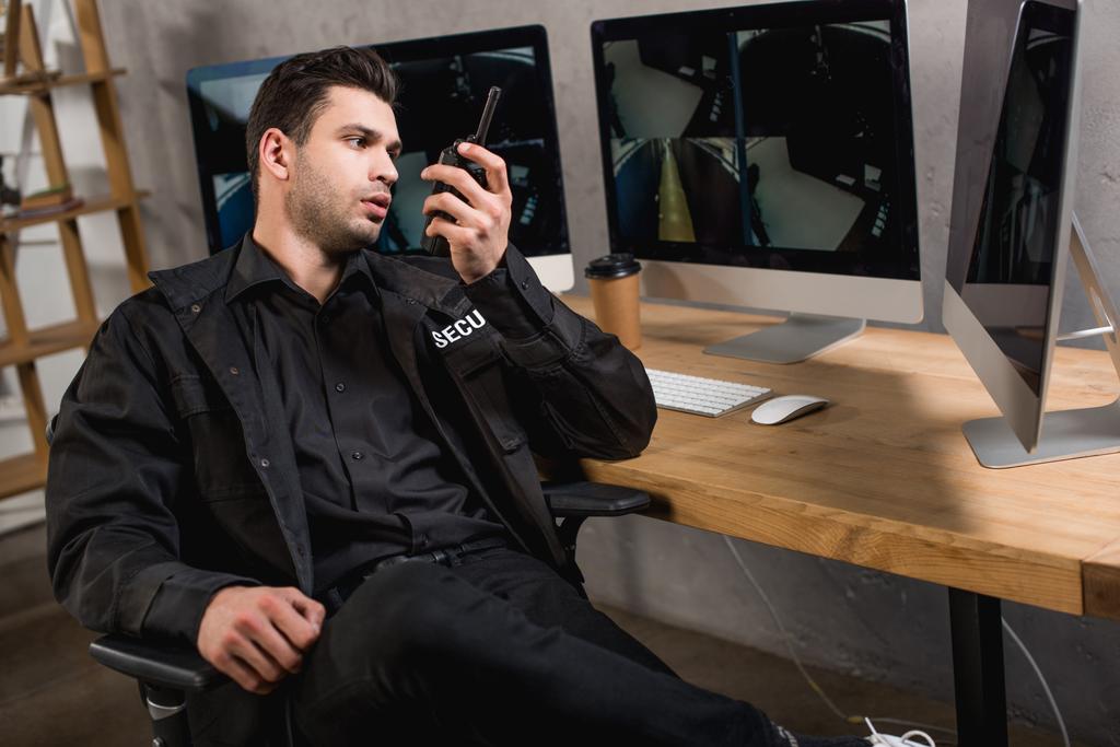 guapo guardia en uniforme hablando en walkie-talkie en el espacio de trabajo
 - Foto, imagen