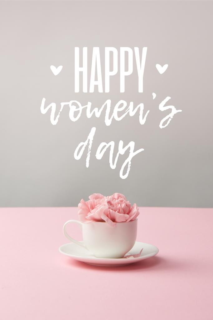 幸せな女性の日のレタリングと灰色の背景に受け皿の白いカップでピンクのカーネーションの花 - 写真・画像
