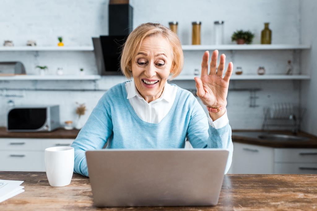 boldog vezető nő integetett a kezével, használ laptop, és miután videó chat a konyha - Fotó, kép