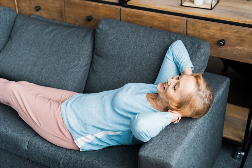 smiling senior woman with hands on head lying and resting on couch - Photo, Image