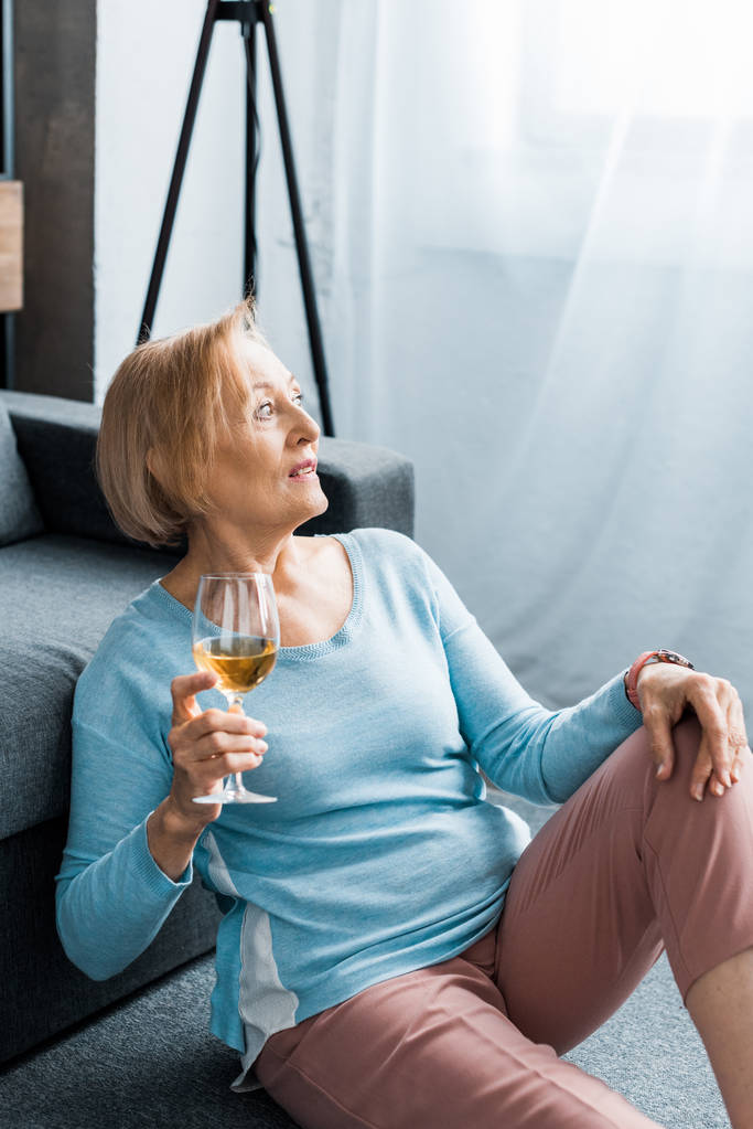 Seniorin sitzt, schaut weg und hält Weinglas zu Hause - Foto, Bild