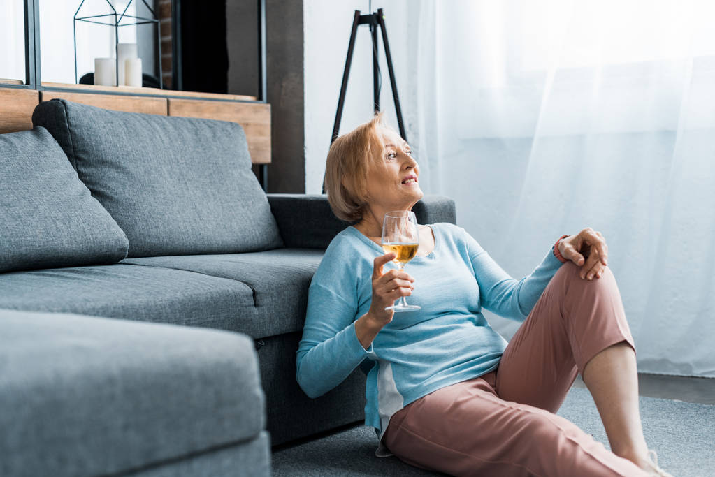 Starší žena sedí a drží sklenka na víno v obývacím pokoji s kopií prostor - Fotografie, Obrázek