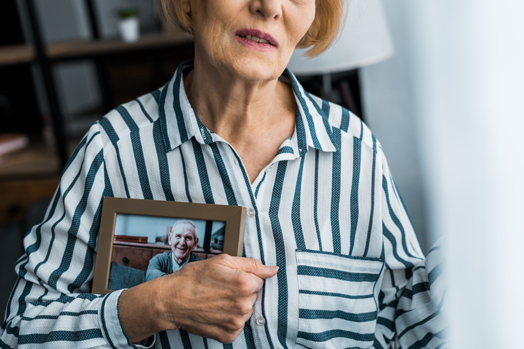 gedeeltelijke weergave van senior vrouw met frame met man op foto thuis - Foto, afbeelding